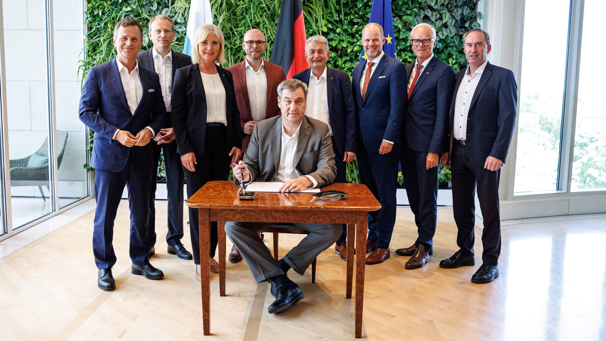 Markus Söder unterzeichnet den Pakt für Berufliche Weiterbildung. Die bayerische Arbeitsministerin Ulrike Scharf und die weiteren Paktpartner stehen hinter ihm.