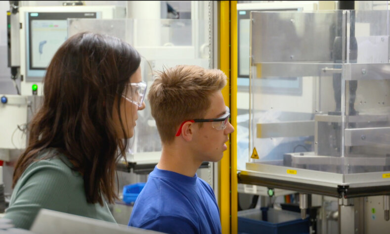 Maschinenbauingenieurin Katharina Wunderlich und ein Kollege tragen Schutzbrillen und blicken auf Gerätschaften.