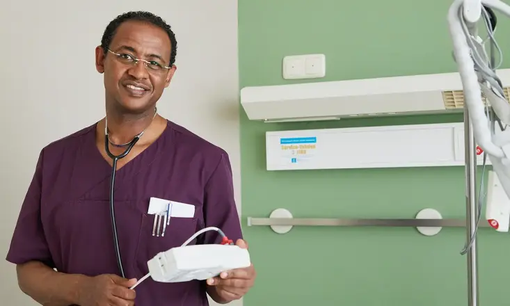 Yadeta Obsa trägt auberginefarbenen Kasack und Stethoskop und lächelt in die Kamera.